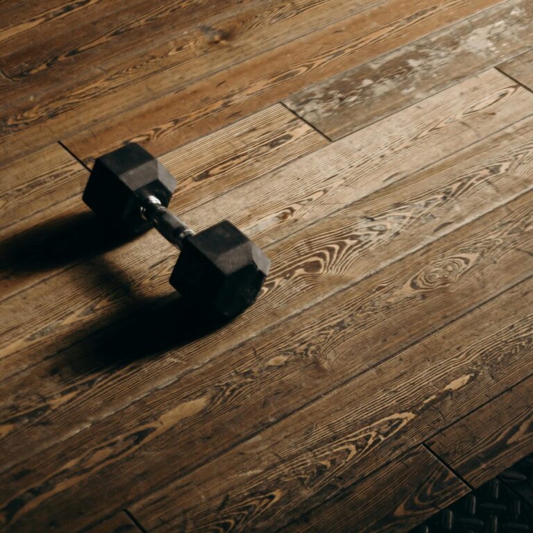A solitary dumbbell rests on a wooden gym floor, offering ample copy space.